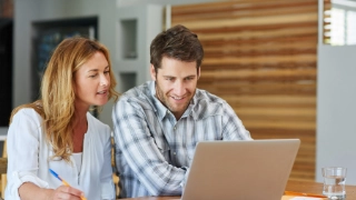 Paar hat Dokumente vor sich und schaut in den Laptop
